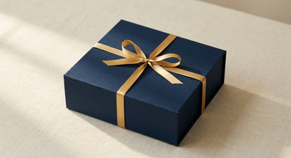 Closed navy gift box tied with a single gold satin ribbon on ivory linen